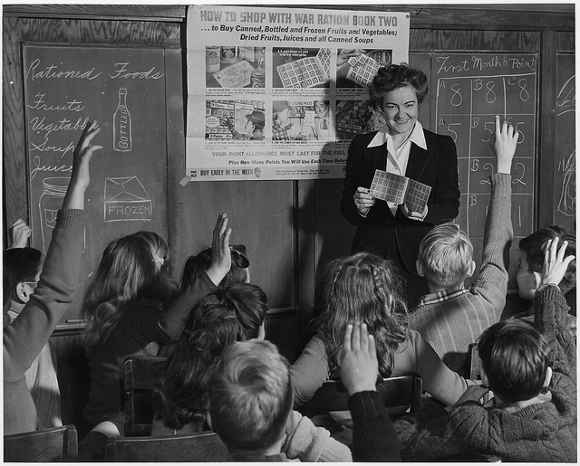 A teacher facing children with raised hands